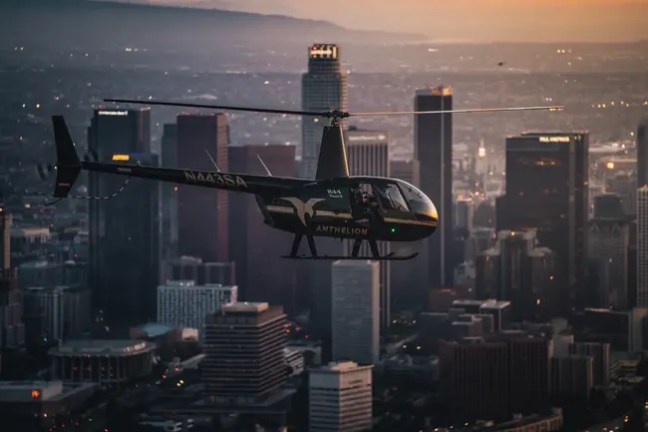 Helicopter flying over a city skyline at sunset.