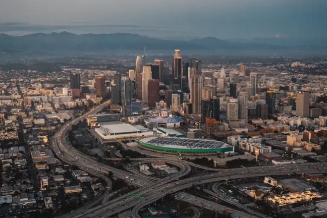Aerial view of cityscape with skyscrapers and intersecting highways at dusk.