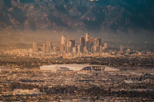 Cityscape with mountains in background and buildings under a cloudy sky.