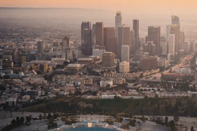Helicopter over city skyline and stadium at sunset.